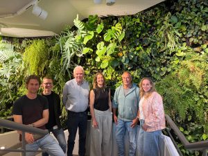 Groep mensen poseren voor een stuk groen. 
